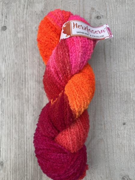 Ein Strang Wolle in kräftigem Pink, Orange und Rot, handgefärbt, liegend auf einem Holzbrett.